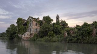 Poveglia Island in the Venice Lagoon at dusk, abandoned brick ruins and bell tower reflected in lagoon water